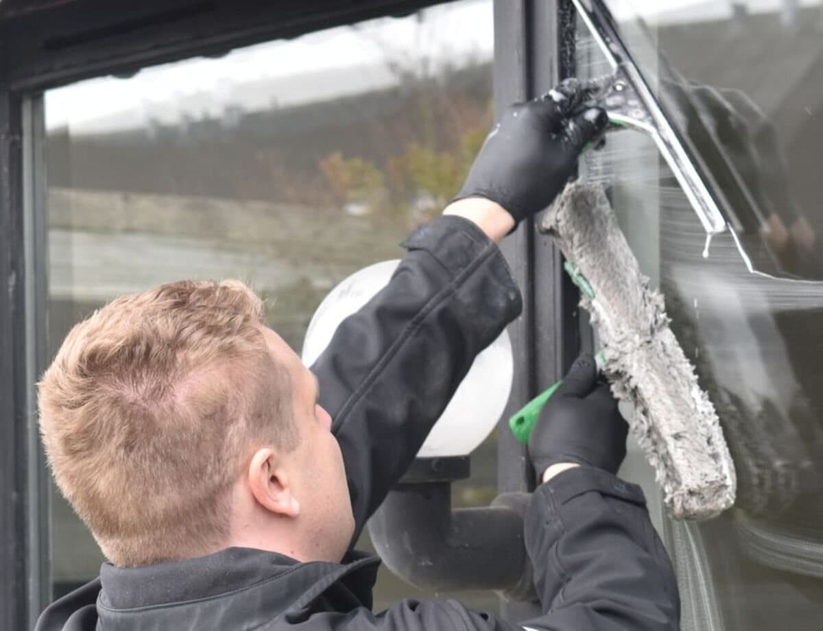 A window cleaner using a scrubber and squeegee to clean the large glass doors of a home